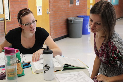 Two female students reading and talking at a table.