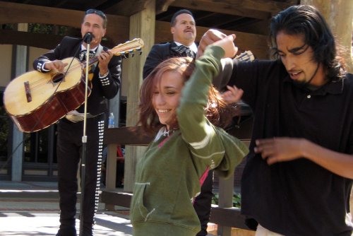 A male and female student smile as they dance to a Mariachi band.