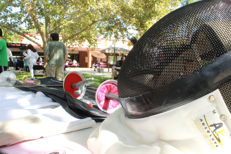 A fencing mask and swords rest on a table outside in the Quad.