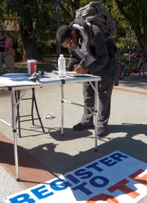A male student signing paperwork on a table outside in the quad.