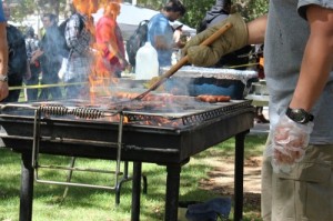 A barbecue grill is smoking and being attended to by a male student.