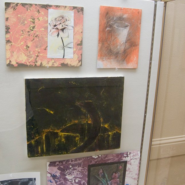 A glass display case showing various student paintings.