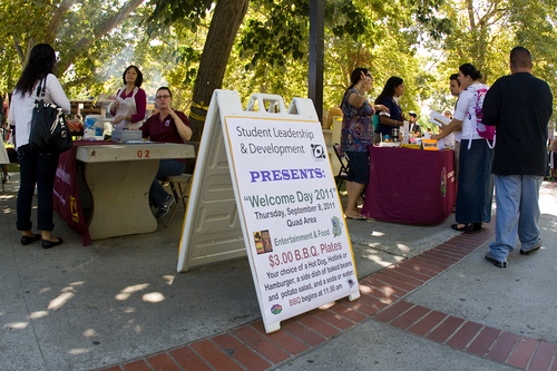Students stand and sit around tables near a Welcome Day sign.