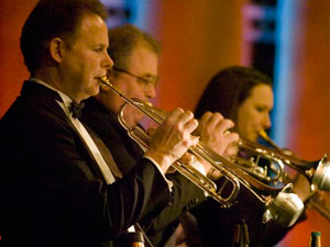 Two men and a woman play are playng horns in a symphony enviroment.