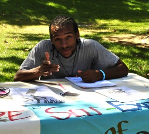 A male student sits at a table in the Quad representing his club on Club Day.