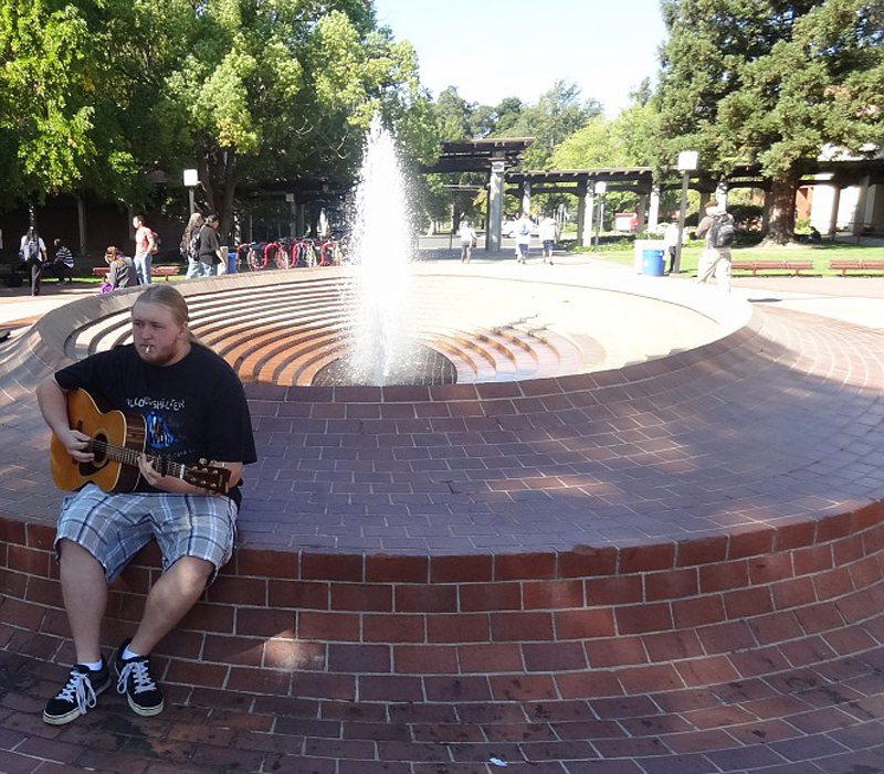 A+man+sitting+on+a+fountain+playing+his+guitar.