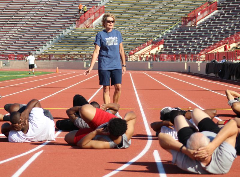 A woman instructs a group of students stretching on the track at Hughes Stadium.
