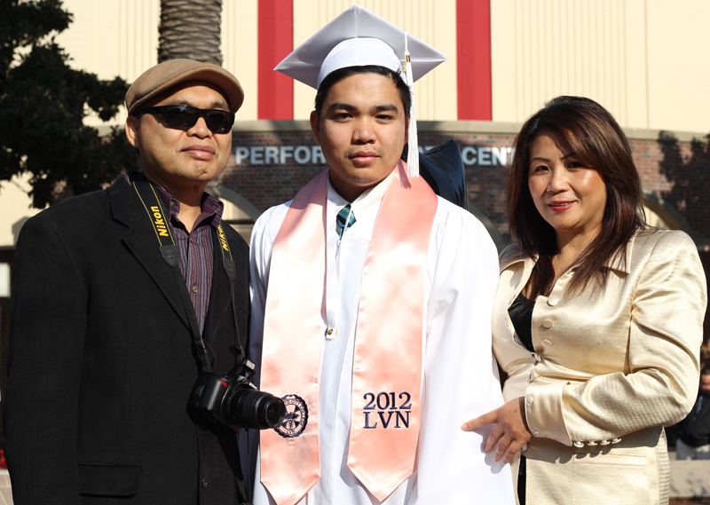 A male student stands with his parents at his graduation ceremony.