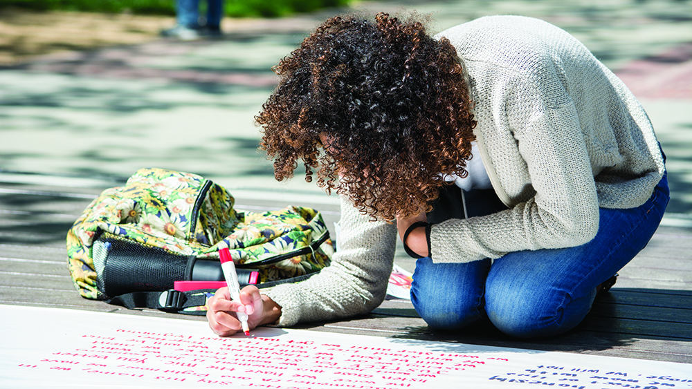 Psychology major Jyonna Land writes out her thoughts Monday, regarding the fatal police shooting of Stephon Clark, on one of the large banners set up out front of the student center.  Jason Pierce | News Editor | jpierce.express@gmail.com