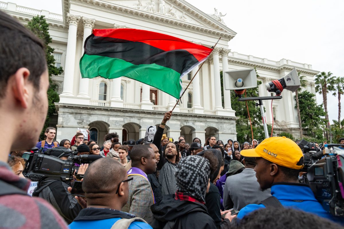 Andre Young, Cousin to Stephon Clark, waving the RBG flag above the crowd of demonstrators gathered at the California State Capitol | Stephon Clark Demonstration | Sacramento, CA  | Thursday 03-07-2019 | Photo by Niko Panagopoulos | Staff Photographer | npanagopoulos.express@gmail.com
