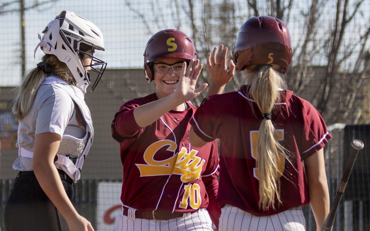 City College Shelby Lloyd (5), right, high fives Jordyn Farren (10), center, after she scores sliding into home in the bottom of the first inning against Lassen College in game two of a doubleheader at The Yard at City College Tuesday, Feb. 18, 2020. Farren has three hits in four at bat and six RBIs in the game. City College defeated Lassen College 16-2. (Sara Nevis/snevis.express@gmail.com)