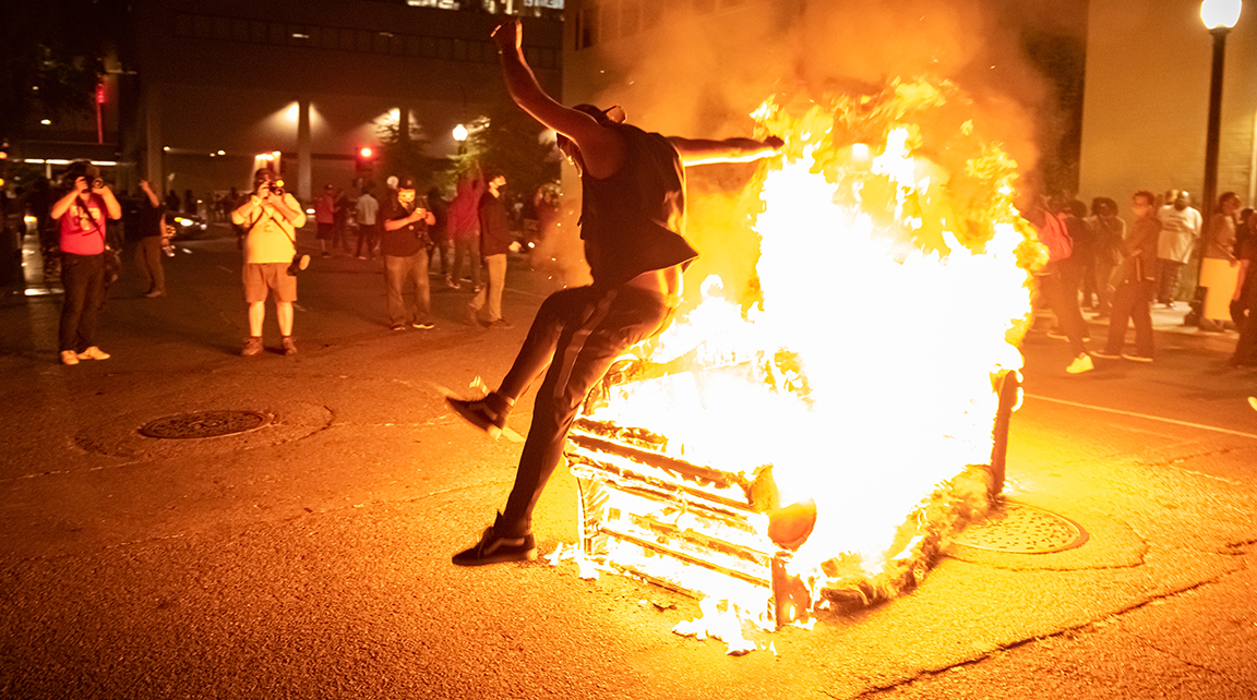 A man jumps over the side of a couch left burning in the street near the county jail during a protest in Sacramento, California, Saturday, May 30, 2020. George Floyd died in Minneapolis Monday after being detained by police. (Niko Panagopoulos/npanagopoulos.express@gmail.com)