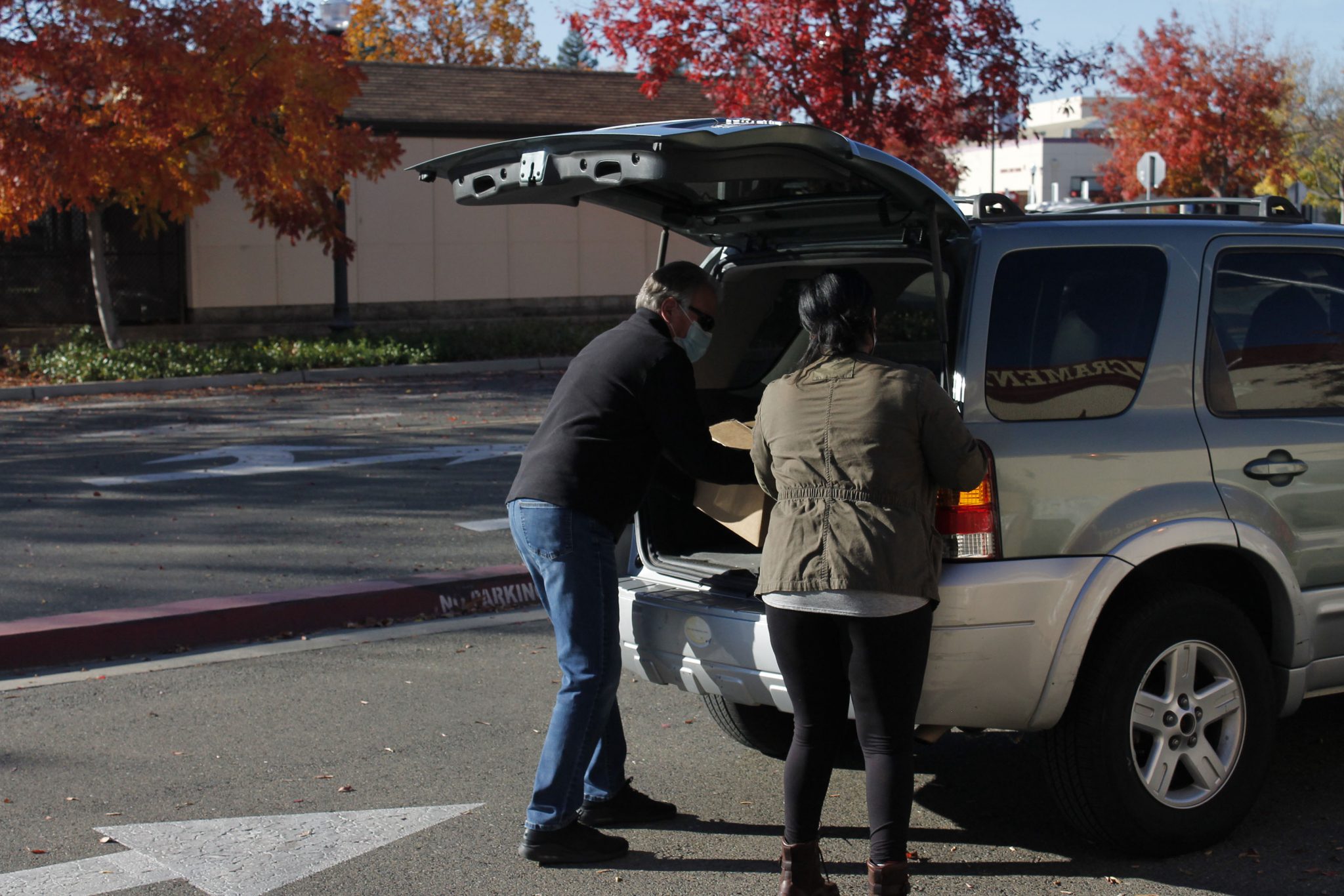 Adjunct assistant photography professor Gordon Lazzarone and R.I.S.E. student support specialist Valerie Lockhart distribute food to a student's trunk while maintaining distance in accordance with COVID-19 protocol. (Shelby Tolly/stolly.express@gmail.com)