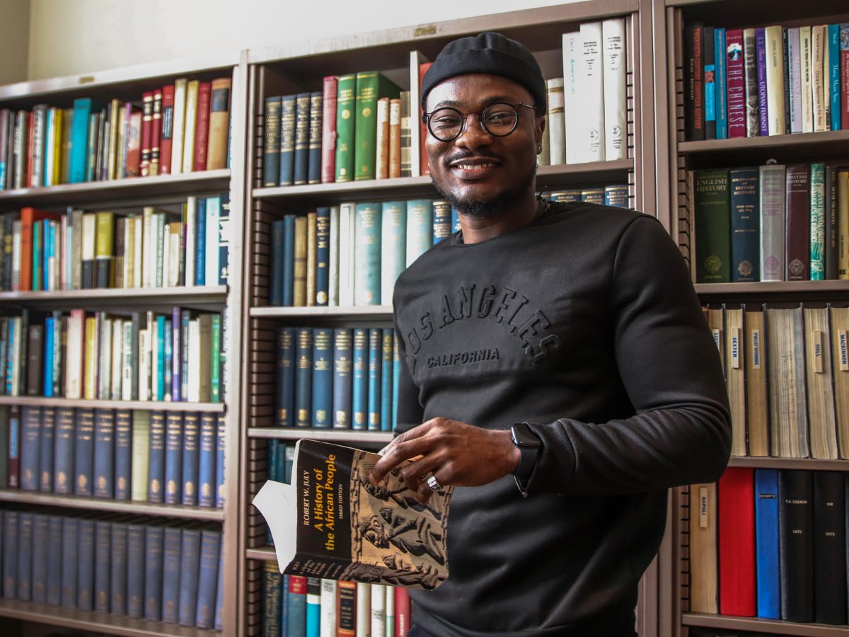 ibrahim Bàbátúndé Anọ́ba, a third-year doctoral UC Davis student, stands in front of a collection of history books located in the library of the UC Davis Department of History.